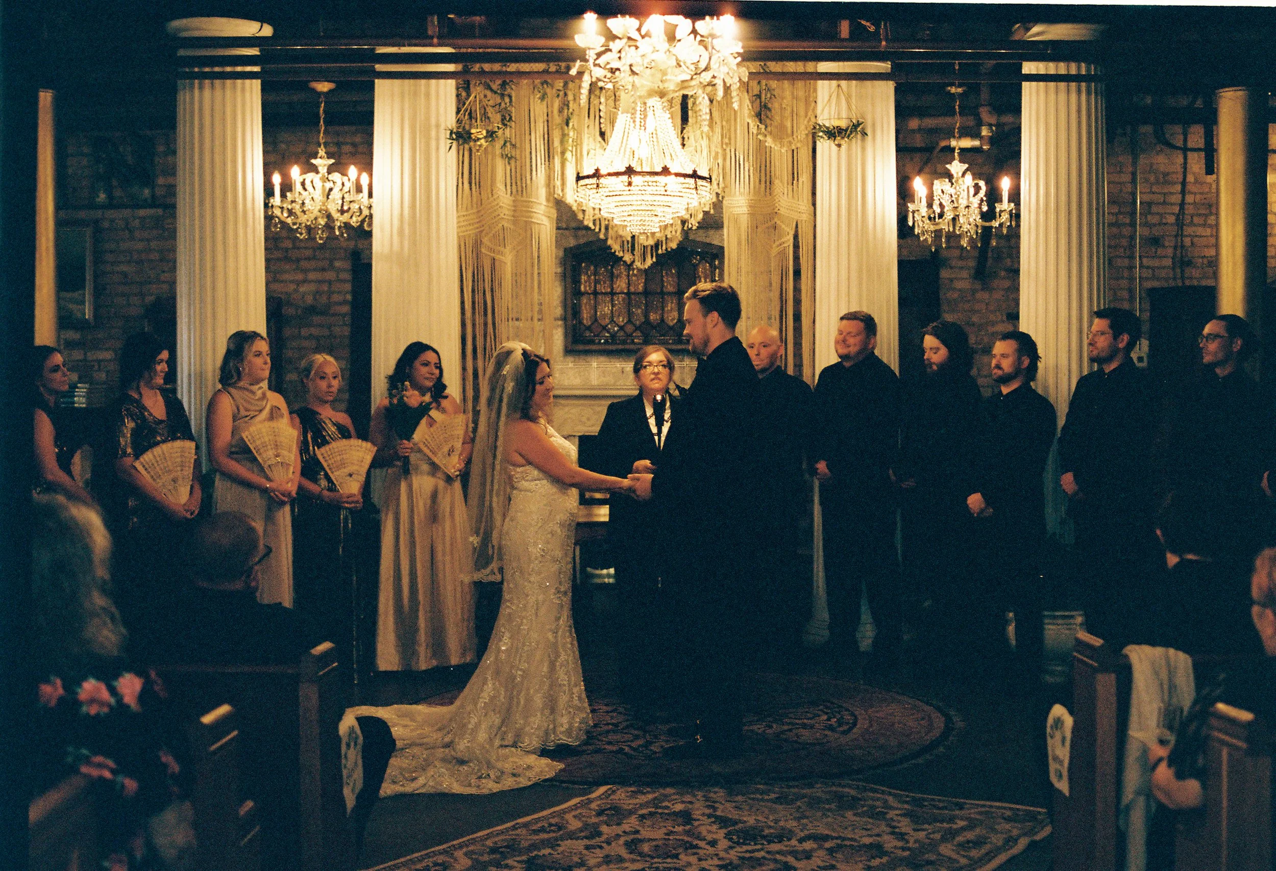 Wedding ceremony under chandeliers and draped fabric at Salvage One with guests gathered around