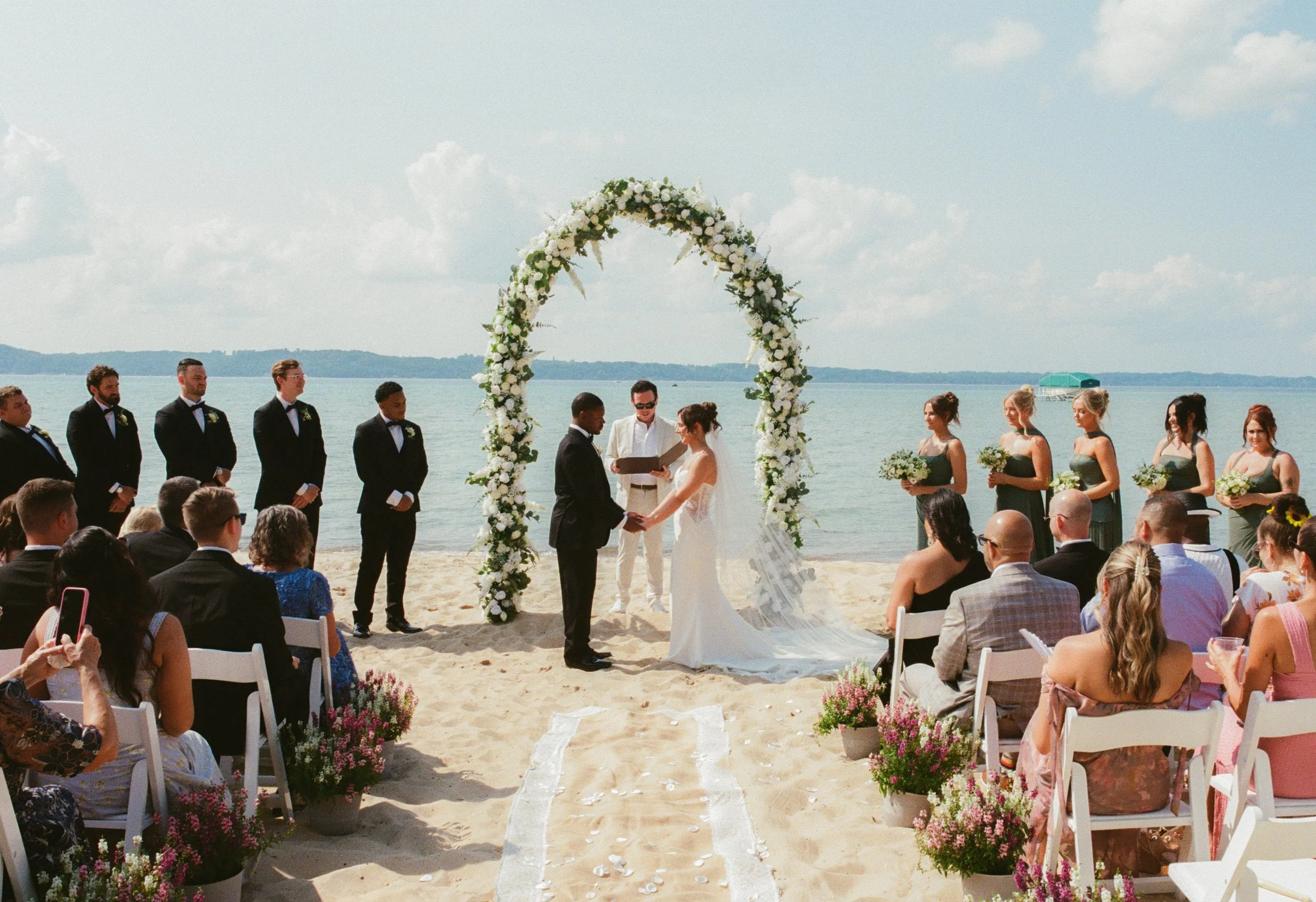Bride and groom exchanging vows beneath a white floral arch overlooking the lake.