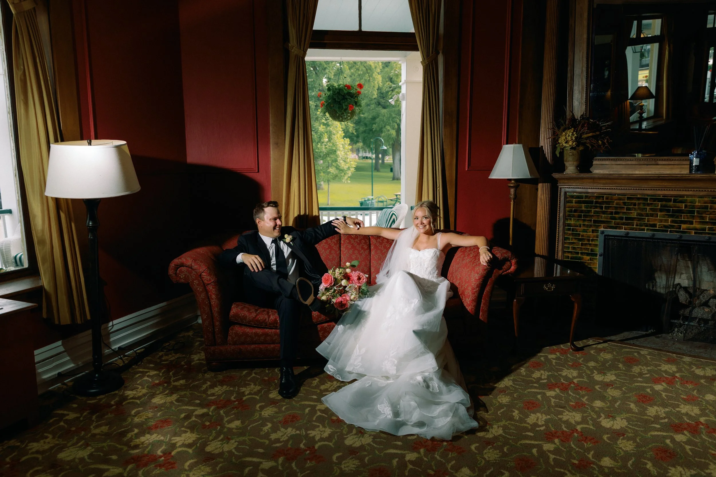Bride and groom relaxing on a vintage red couch inside Stafford's Perry Hotel during wedding portraits.