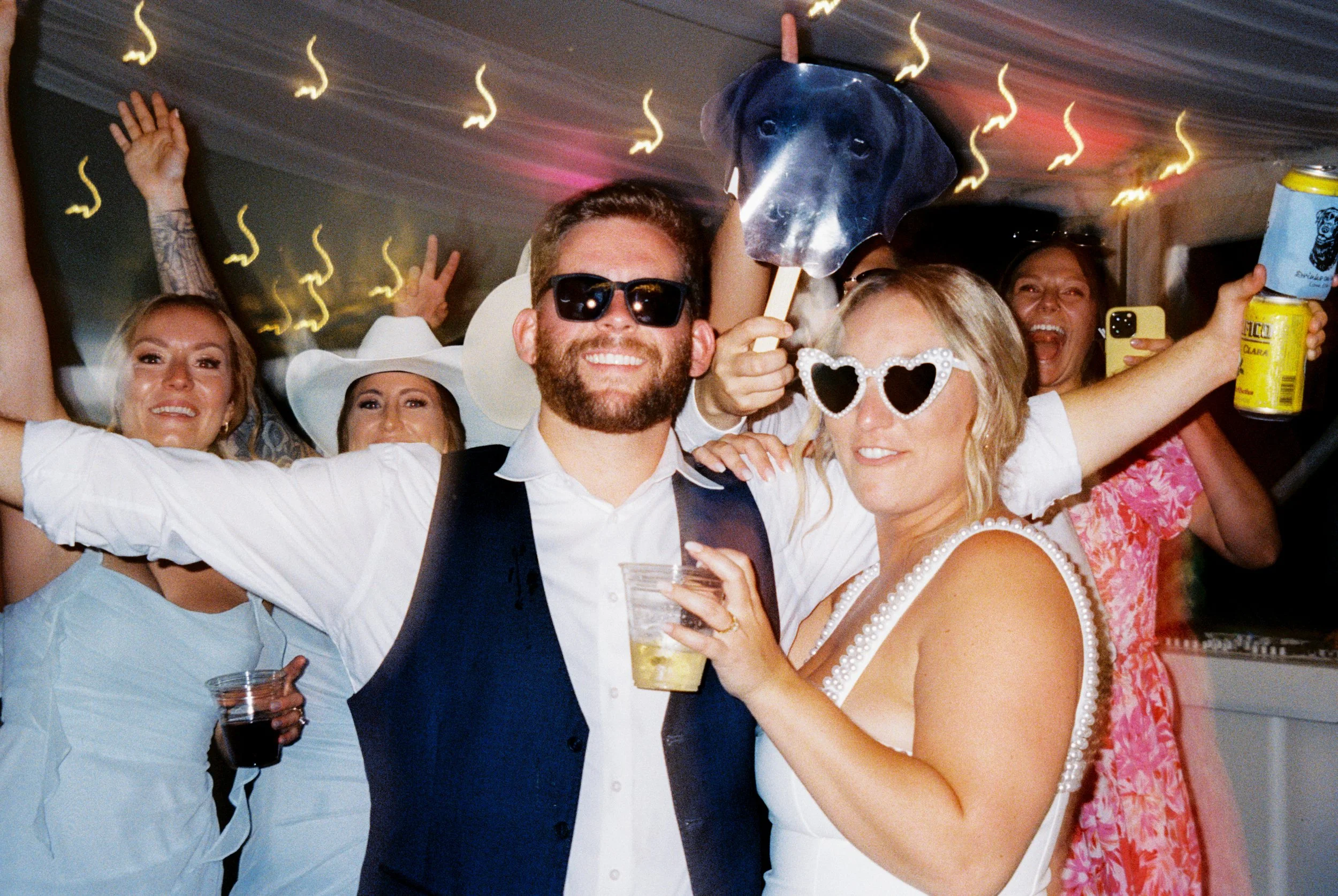 Bride and groom wearing fun sunglasses while celebrating with friends during their wedding reception.