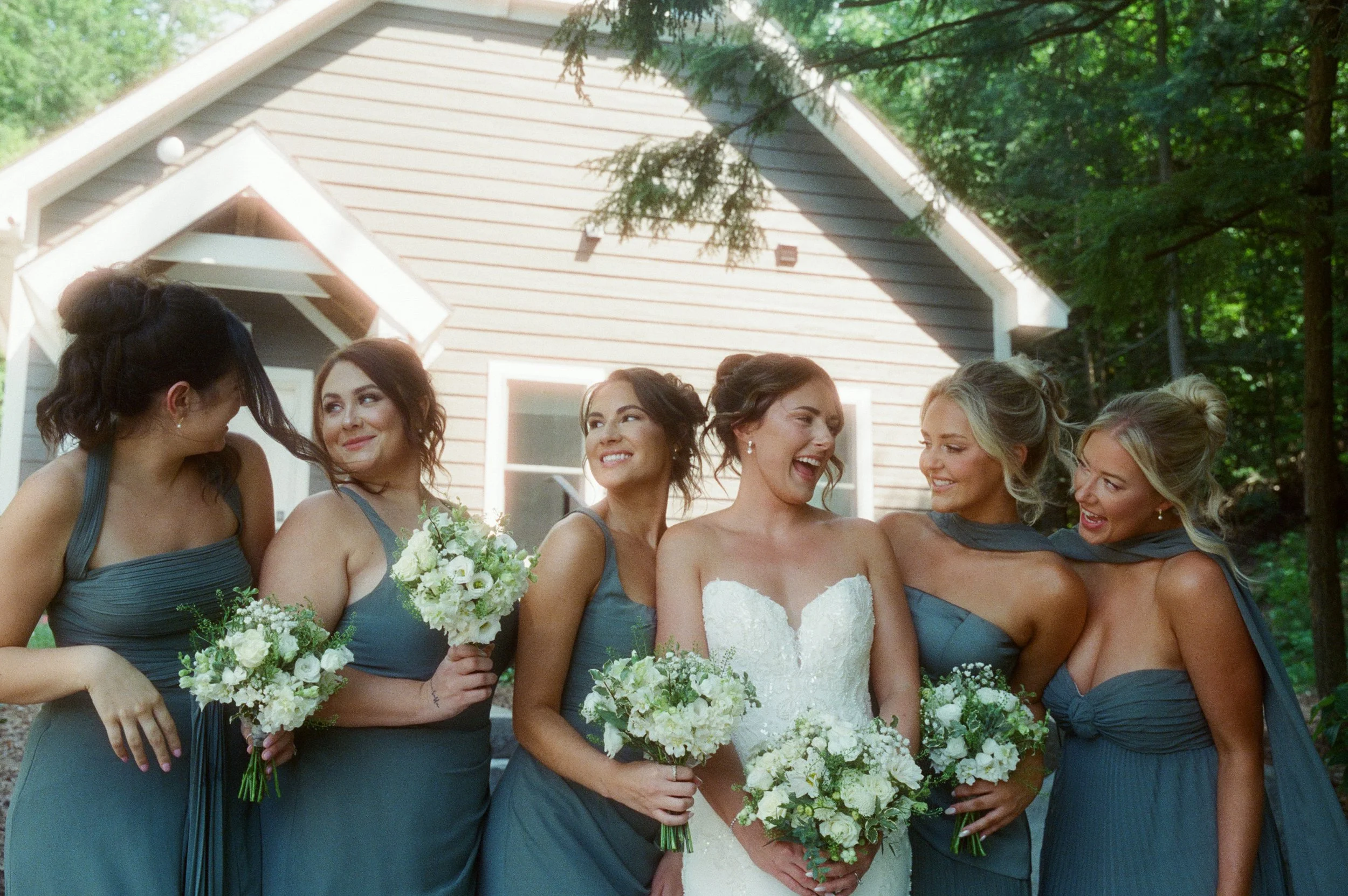 Bride laughing with her bridesmaids in green dresses during a Northern Michigan backyard wedding.
