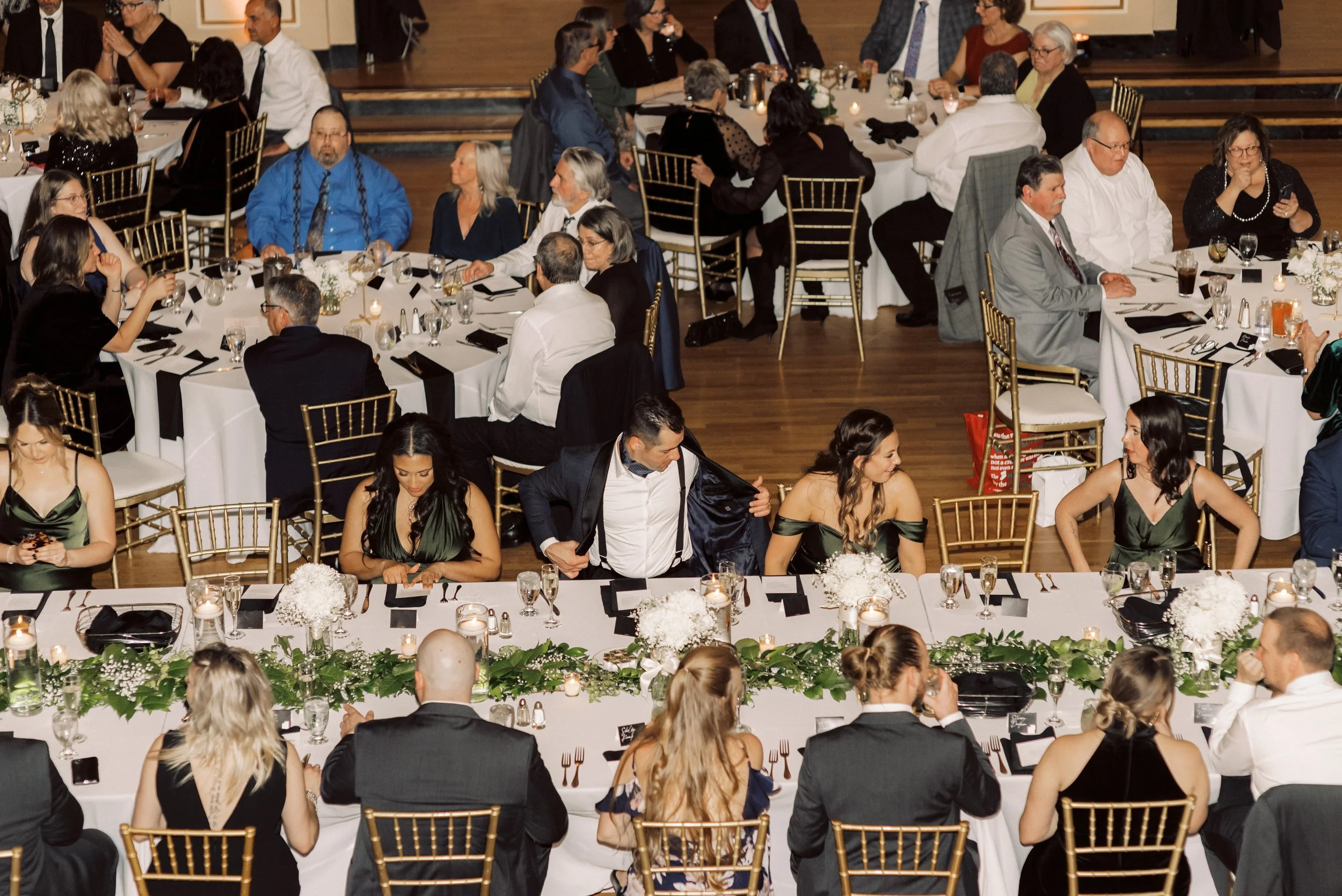 Wedding guests seated around long reception tables with white florals, greenery, and candlelight during a downtown Detroit wedding reception.