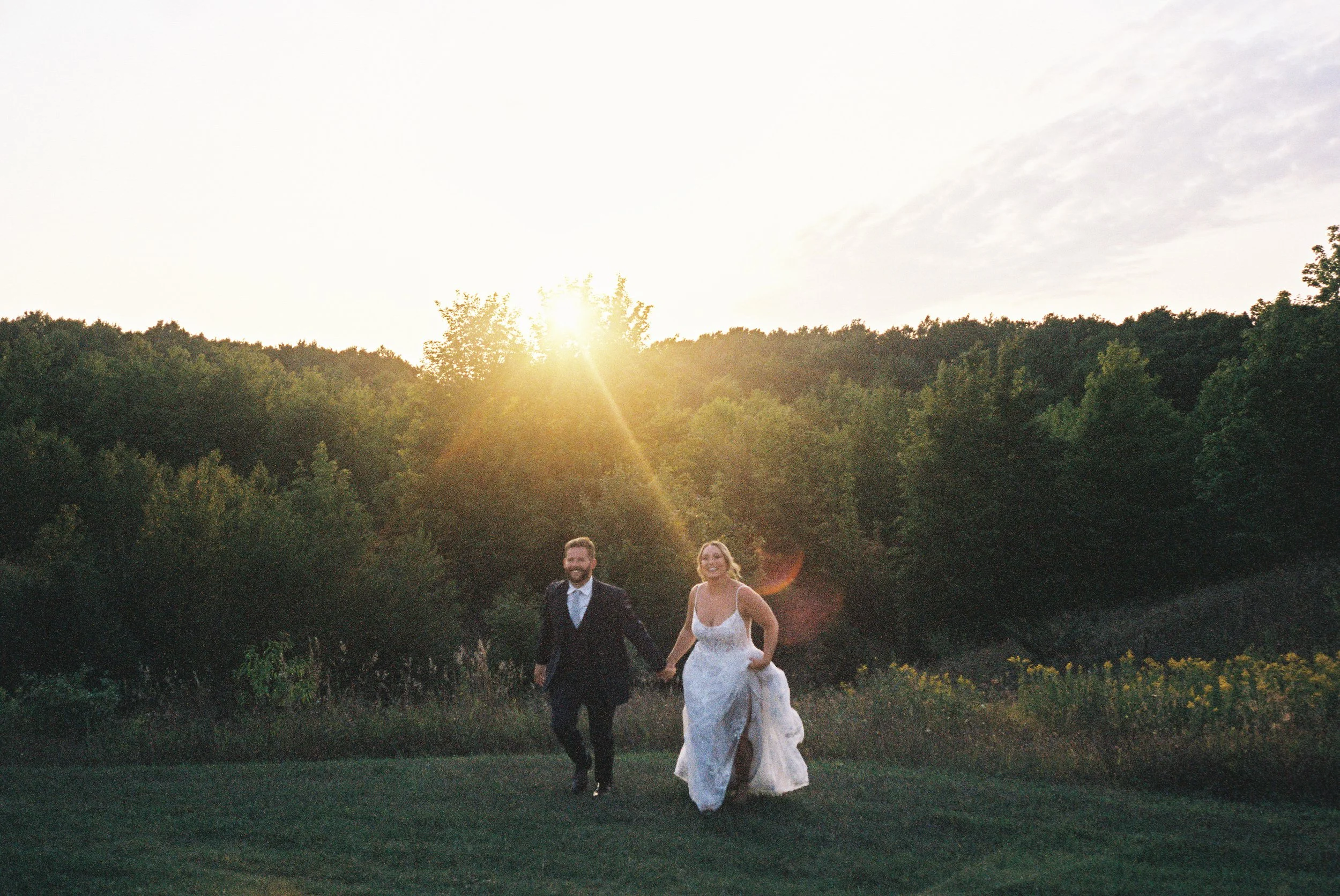 Bride and groom running hand in hand across a field during golden hour portraits at their Northern Michigan vineyard wedding.