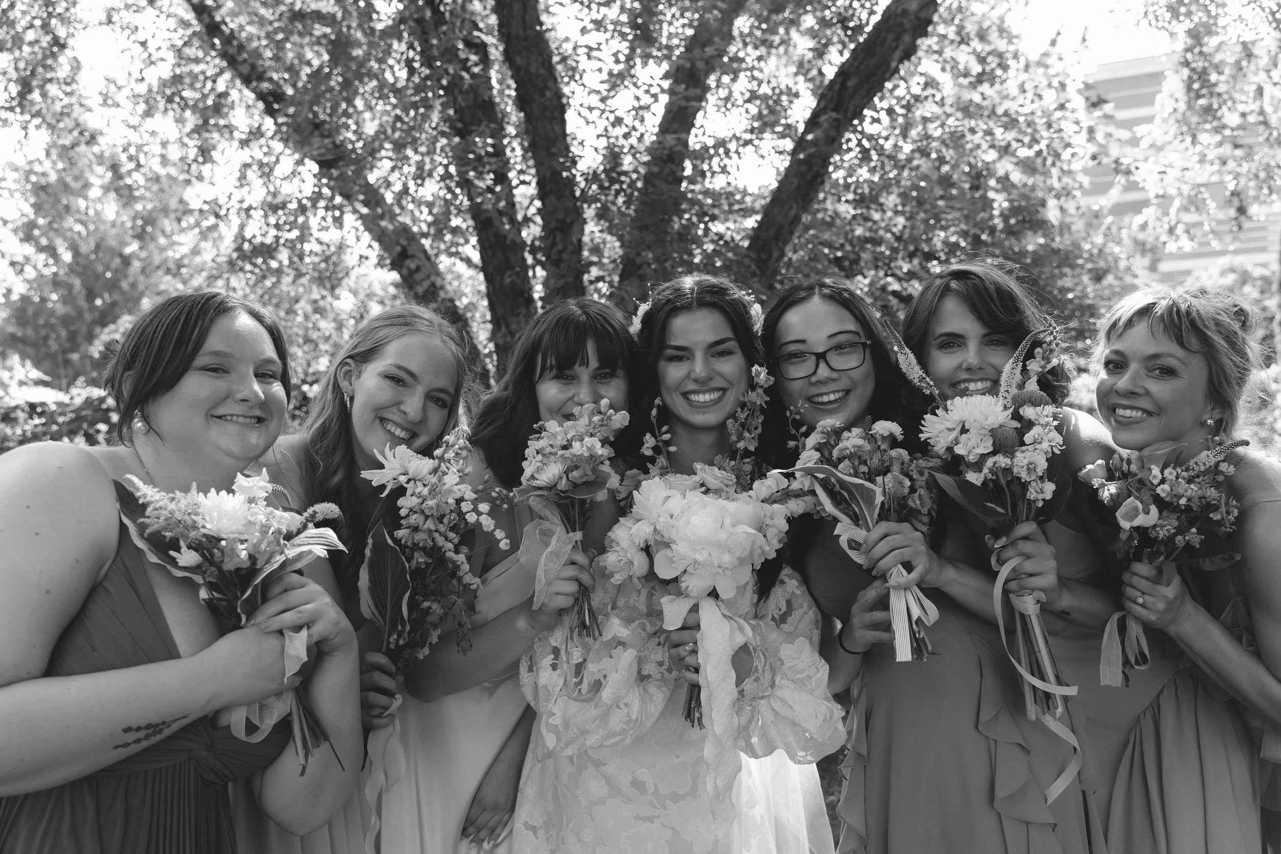 Black and white photo of bridesmaids smiling and holding bouquets together, celebrating during a joyful wedding moment