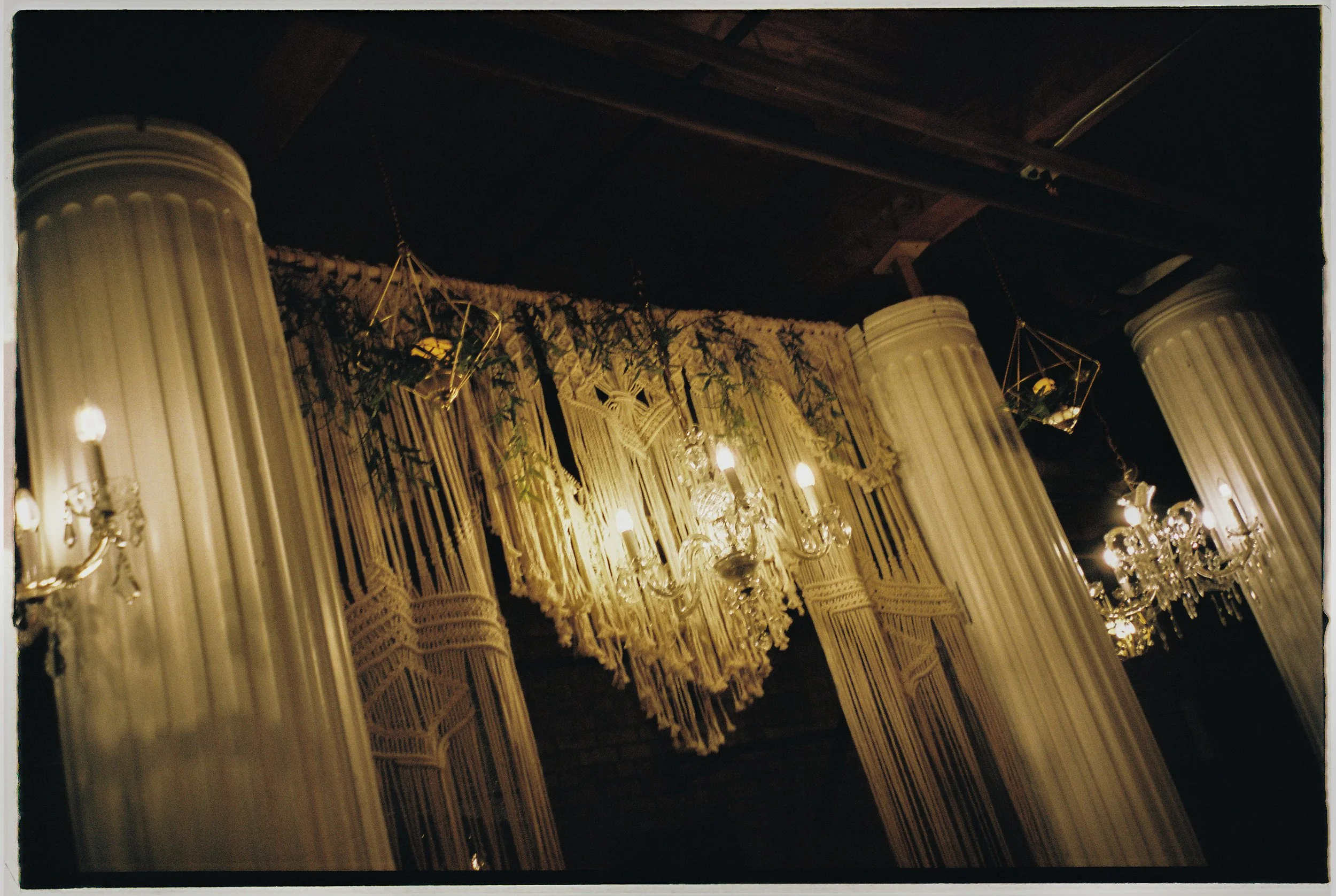 Dramatic reception lighting with chandeliers and macrame decor hanging between columns at Salvage One