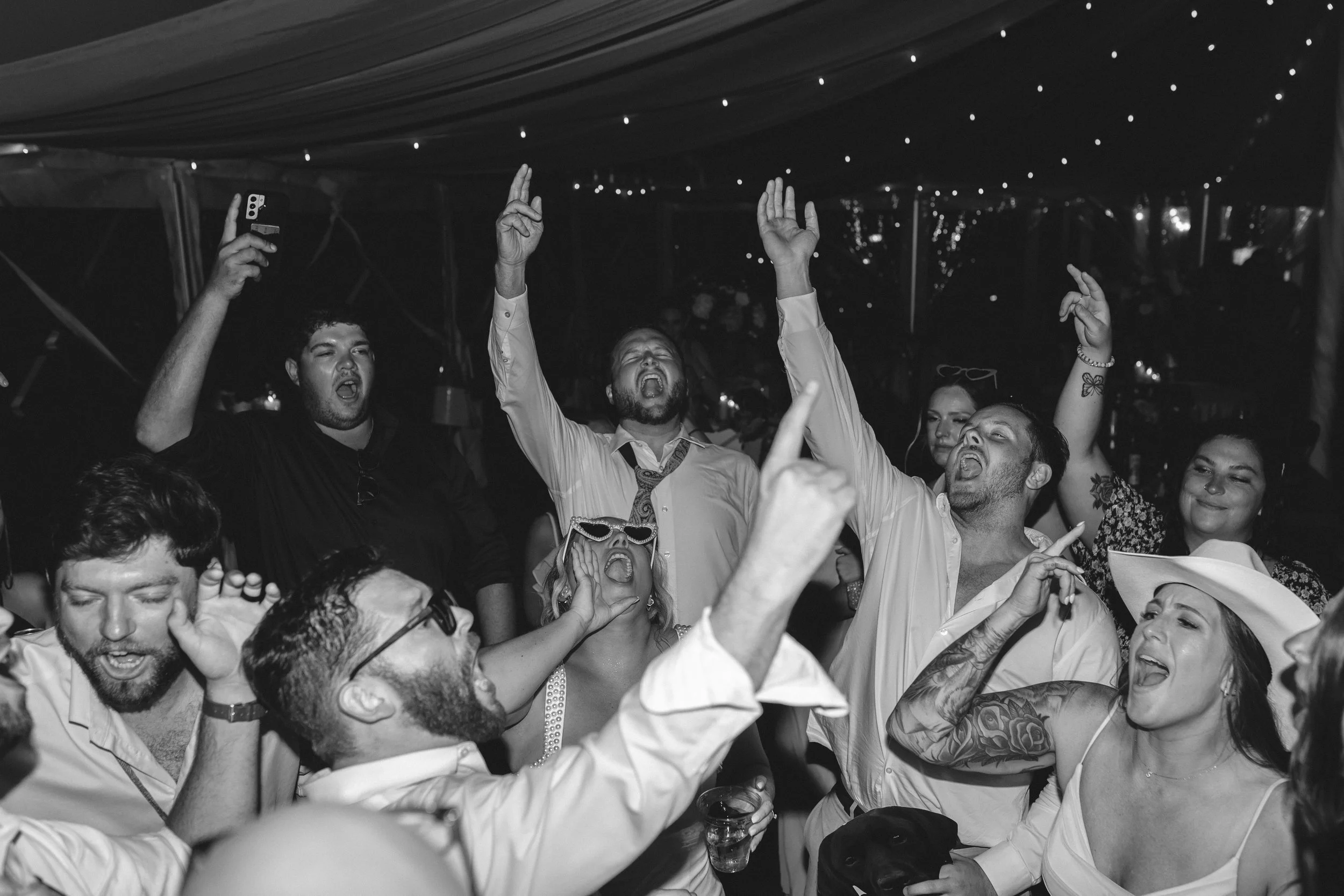 Guests singing and dancing together on a crowded dance floor during an energetic Northern Michigan vineyard wedding reception.