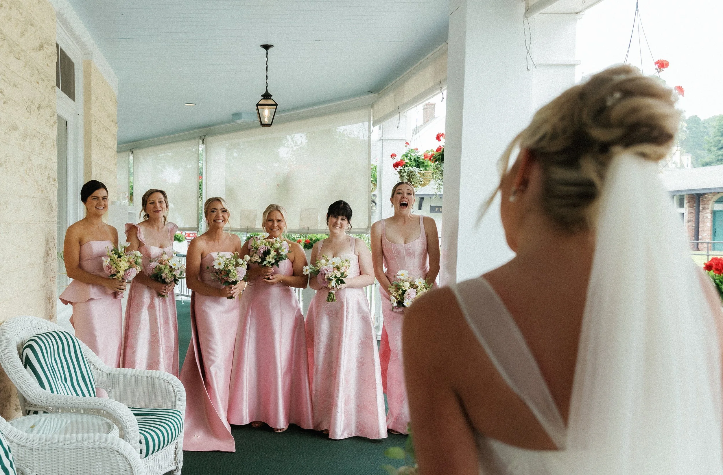 Bridesmaids in blush pink dresses reacting during an emotional first look with the bride.