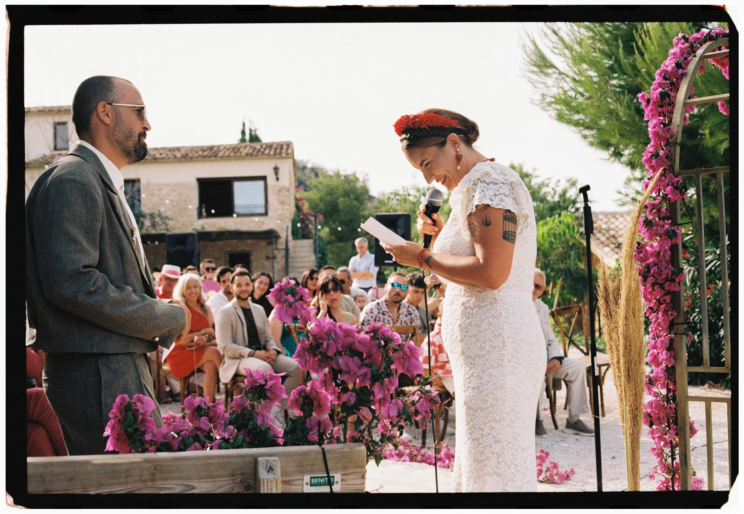 Bride reading heartfelt vows during her Spain wedding ceremony surrounded by vibrant pink florals.