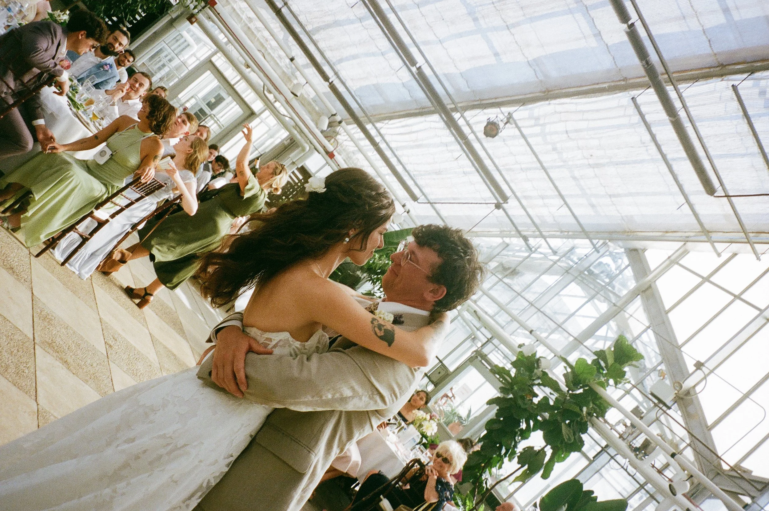 Bride and groom dancing closely inside a greenhouse reception space, captured in candid film wedding photography style