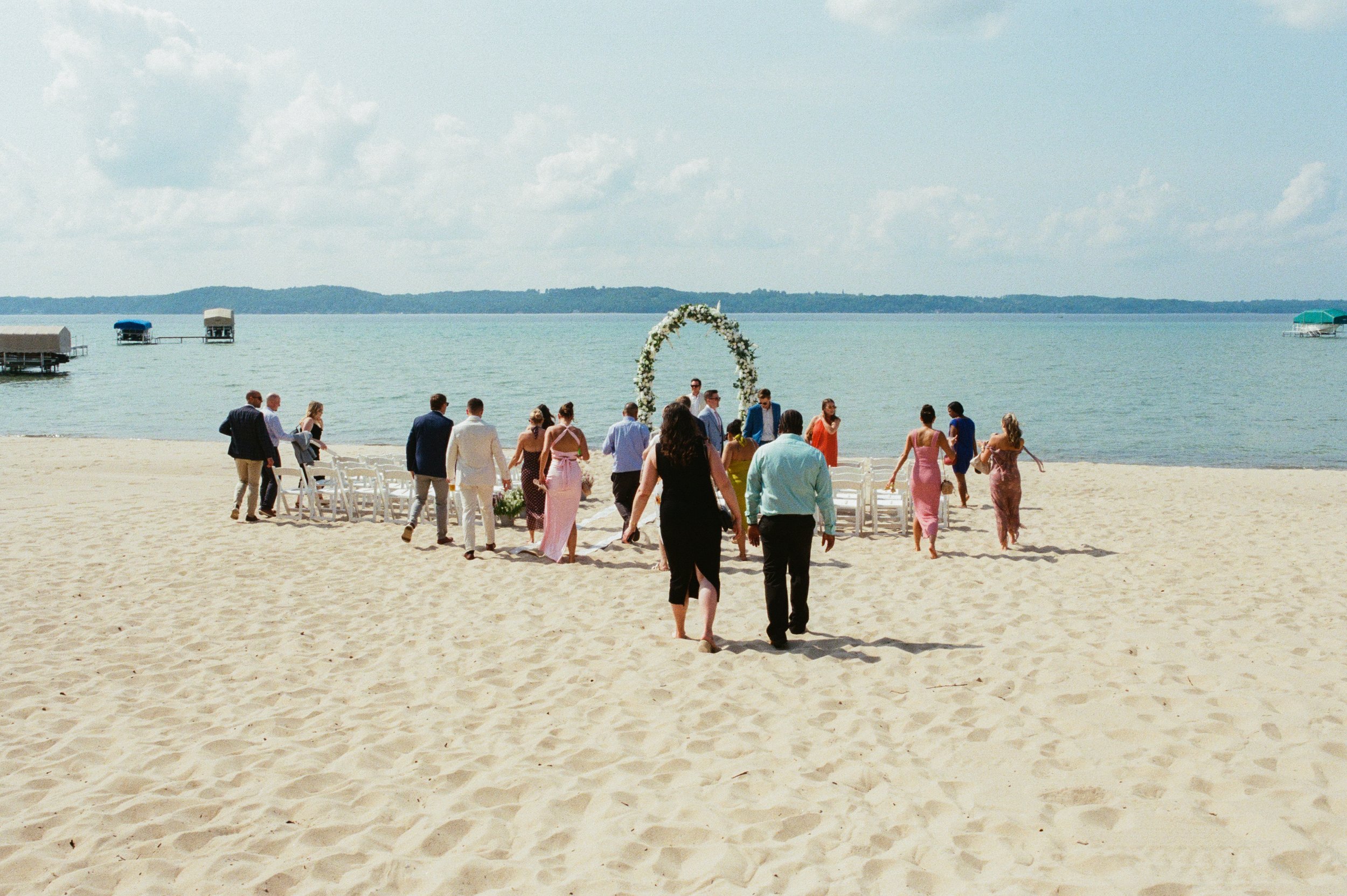 Wedding guests walking toward the floral arch and white chairs for the lakeside ceremony.