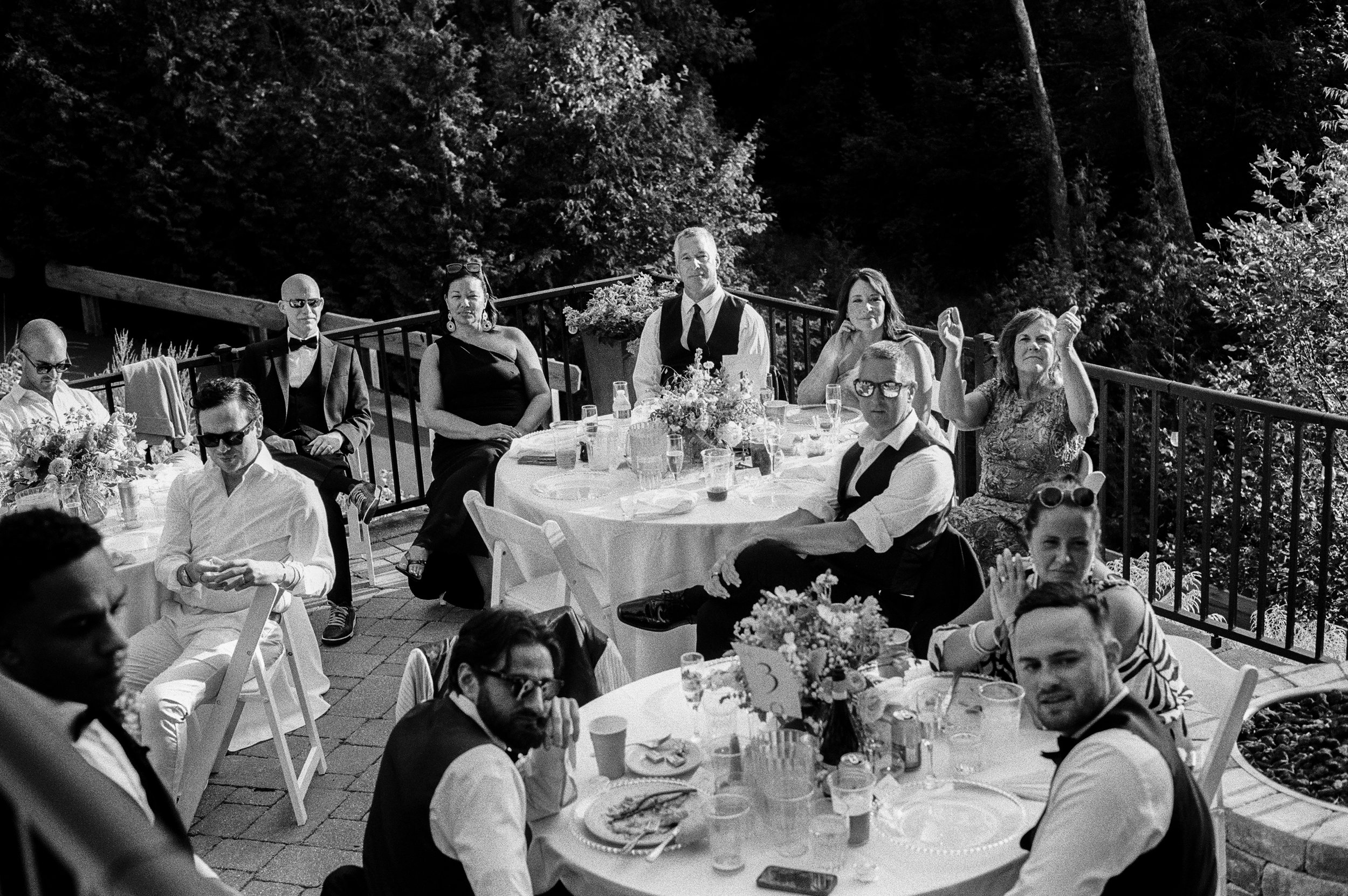 Black and white candid photo of guests gathered around outdoor reception tables.