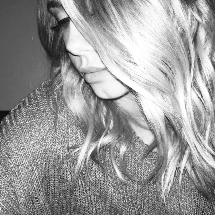 Black and white close-up photo of a woman with long, wavy blonde hair, looking down with a slight smile, wearing a textured sweater.