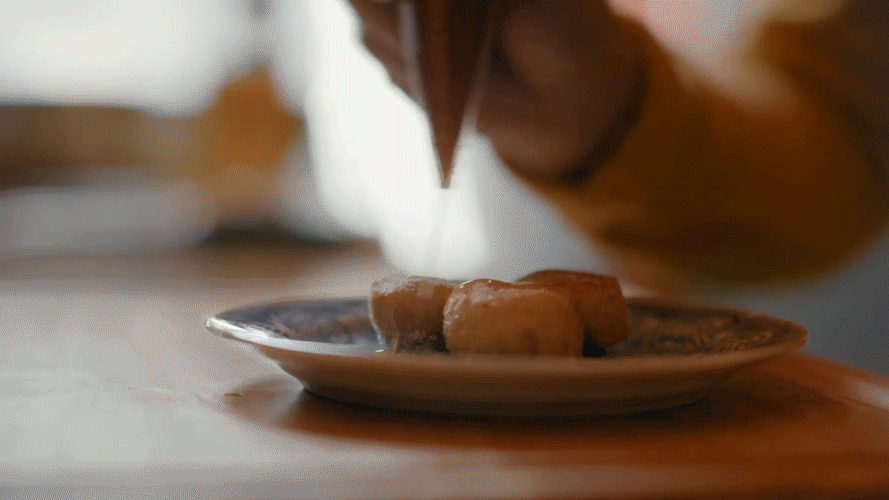 A person is sprinkling cinnamon on a plate of donuts.
