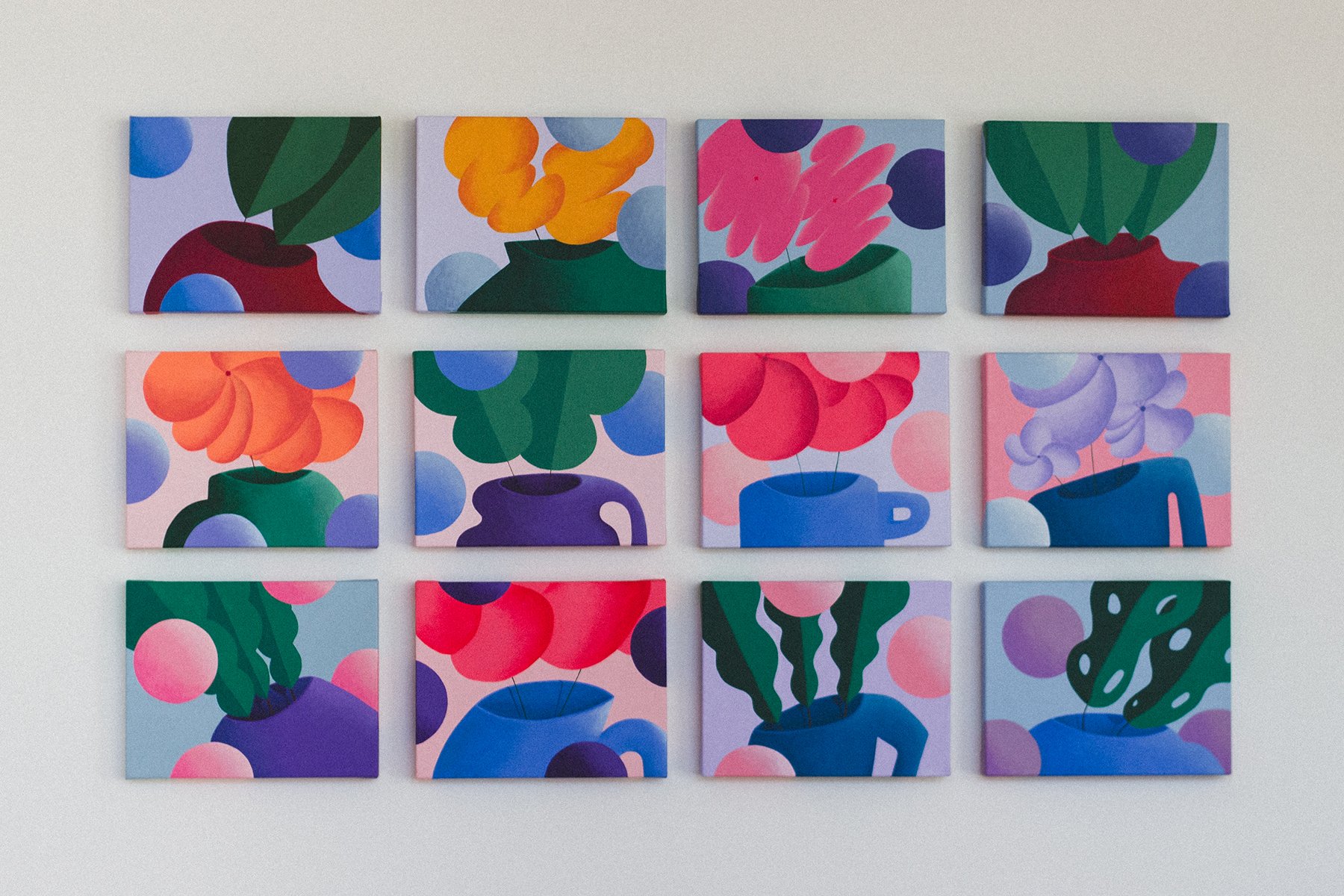 A collection of twelve colorful, abstract floral paintings arranged in a 3x4 grid on a white wall.