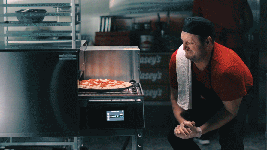 A chef watching a pizza baking in an industrial oven in a commercial kitchen.