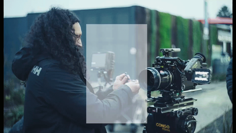 A woman with curly hair operating a professional film camera outdoors.