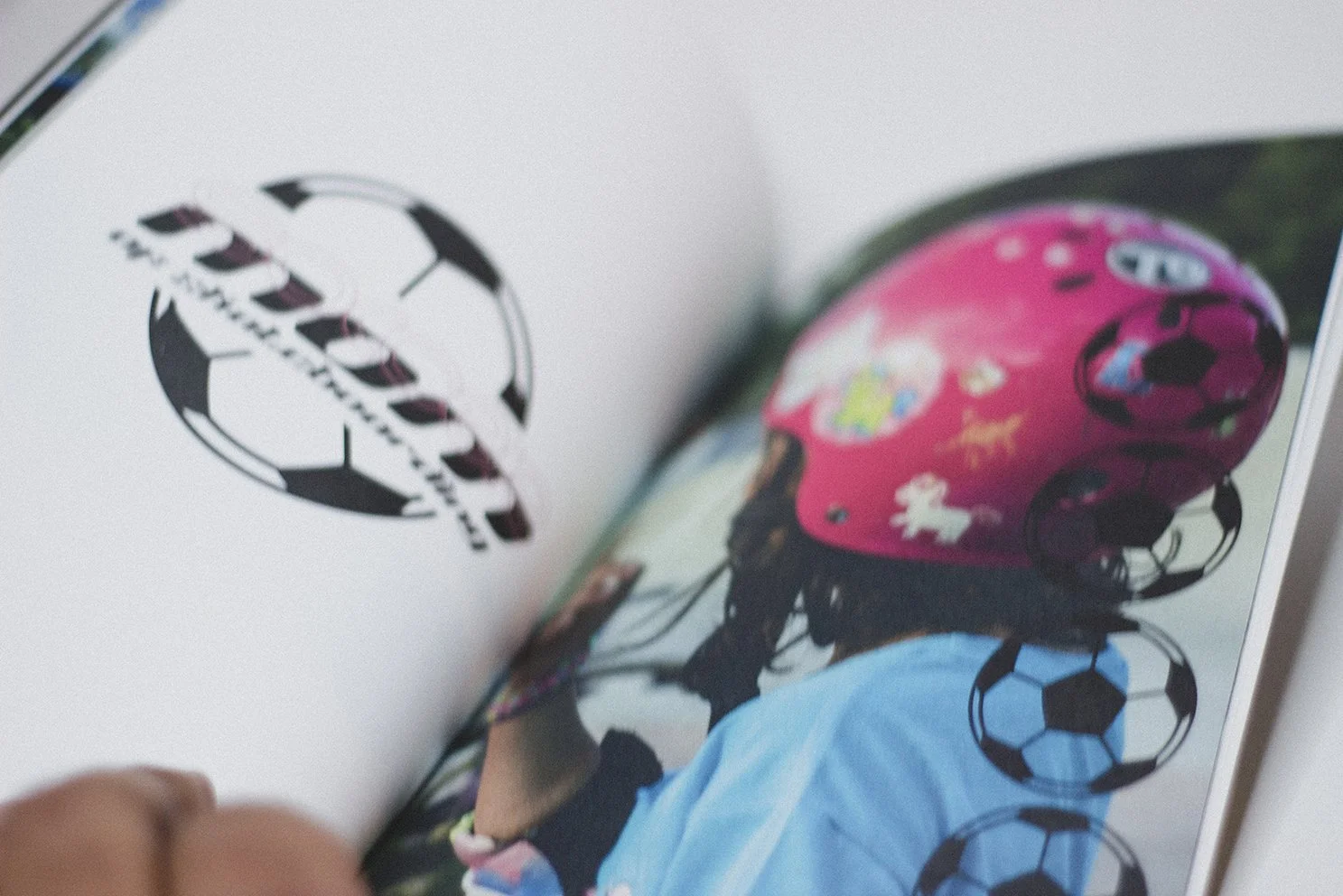 Open magazine with a black and white logo on the left page and a colorful photo of a child wearing a pink helmet decorated with cartoon characters on the right page.
