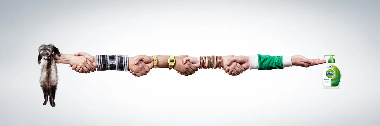 A series of hands holding each other, with the first hand holding a puppy on the left and the last hand pointing to a bottle of Dettol hand sanitizer on the right.