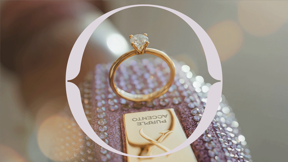 Close-up of a gold engagement ring with a diamond, placed on a decorated surface with rhinestones and a perfume box in the background.