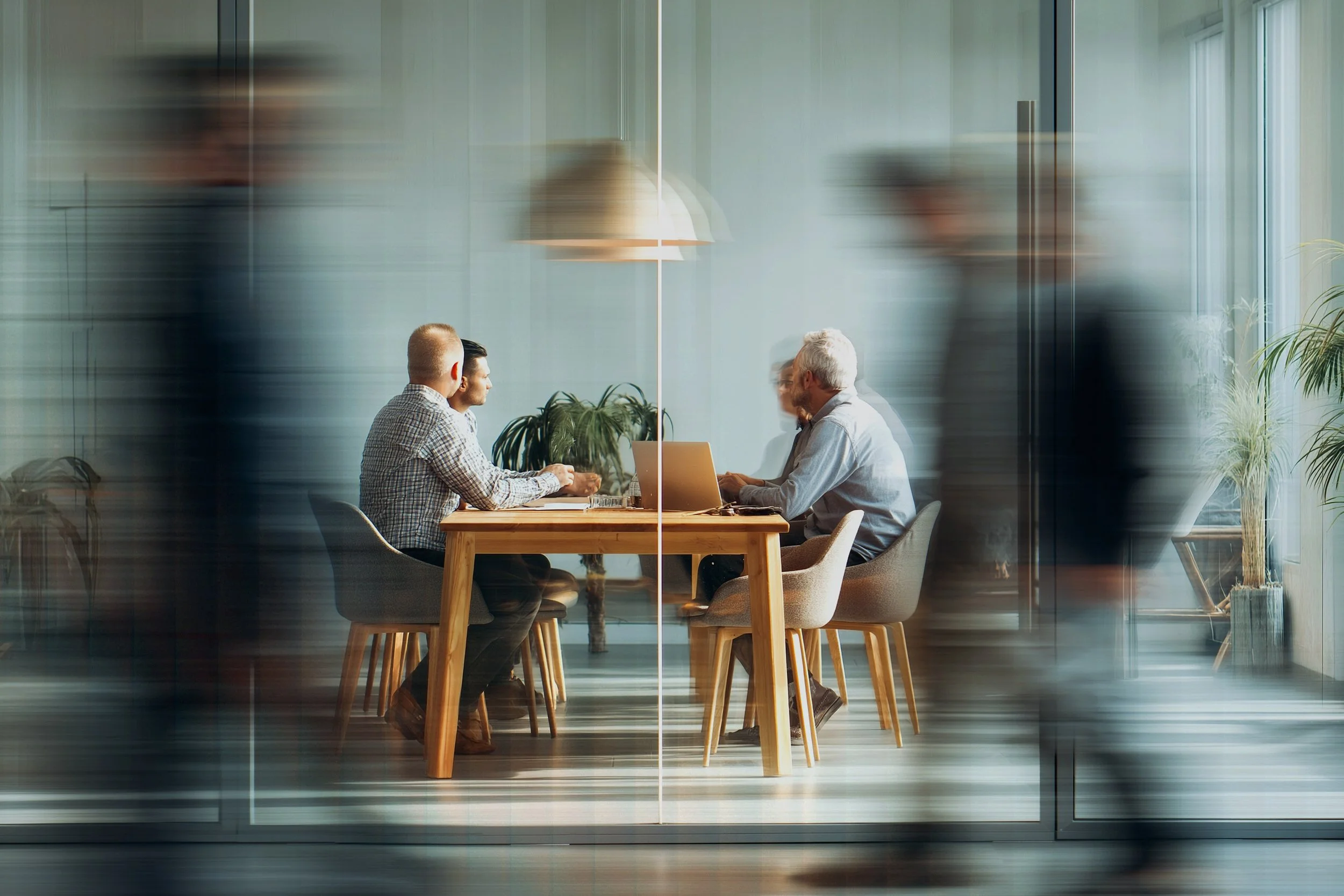 People in a business meeting seen through a glass wall with motion blur of passing pedestrians.
