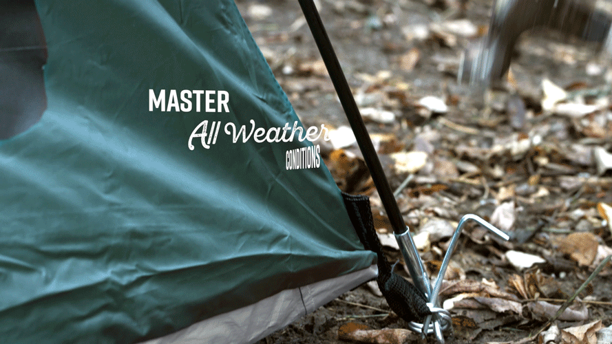 Close-up of a green tent with the words "Master All Weather Conditions" printed on it, set up outdoors on muddy ground with leaves and twigs, and a metal tent stake anchoring the fabric.