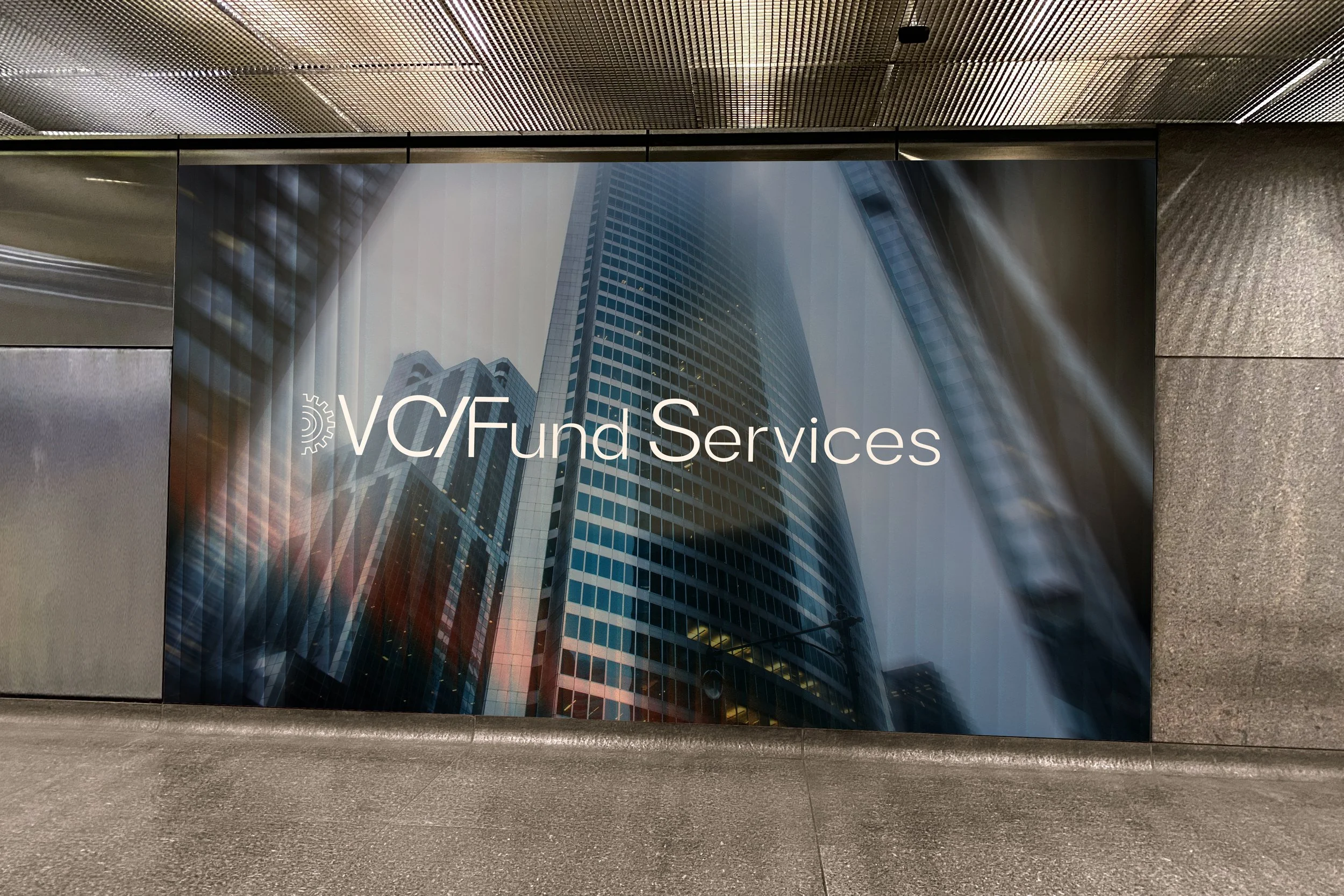 Sign for VC/Fund Services on a building with tall glass skyscrapers reflected on the front