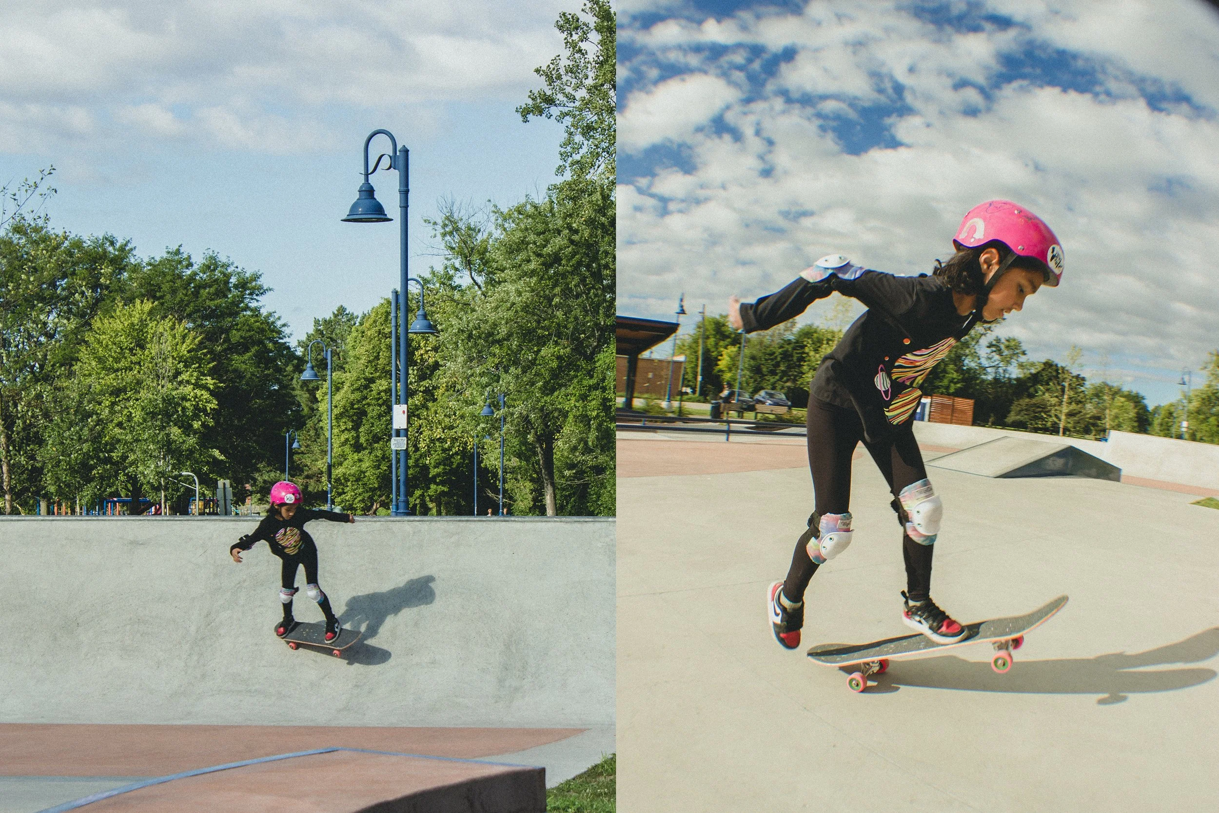 A young girl wearing a pink helmet and protective gear skateboarding in a skatepark on a clear day with a partly cloudy sky.