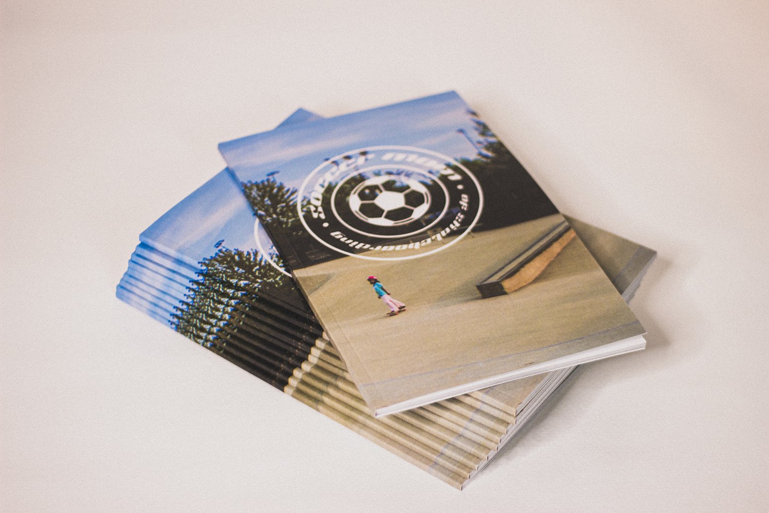 Stack of flyers or brochures with a soccer-themed logo on top with a soccer ball and circular text, and a photo of a woman skateboarding in a park.