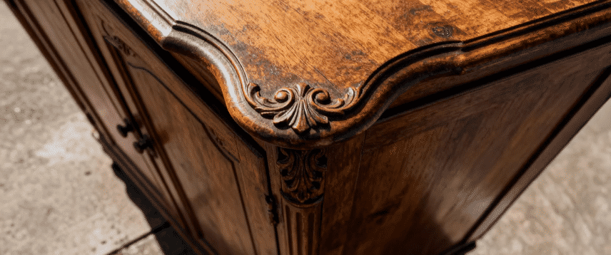 Close-up of an ornate, antique wooden cabinet with carved details on the corner, showing a polished surface and intricate woodwork.