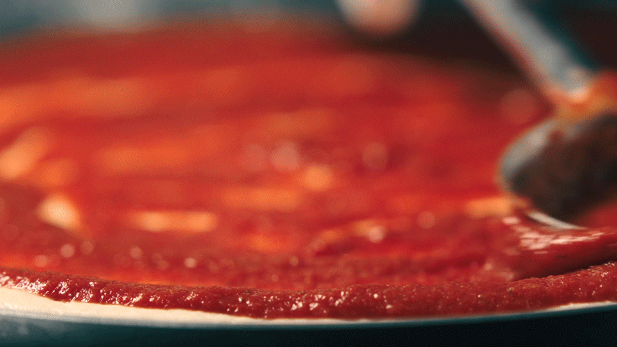 Close-up of a pizza with tomato sauce being spread on the dough.