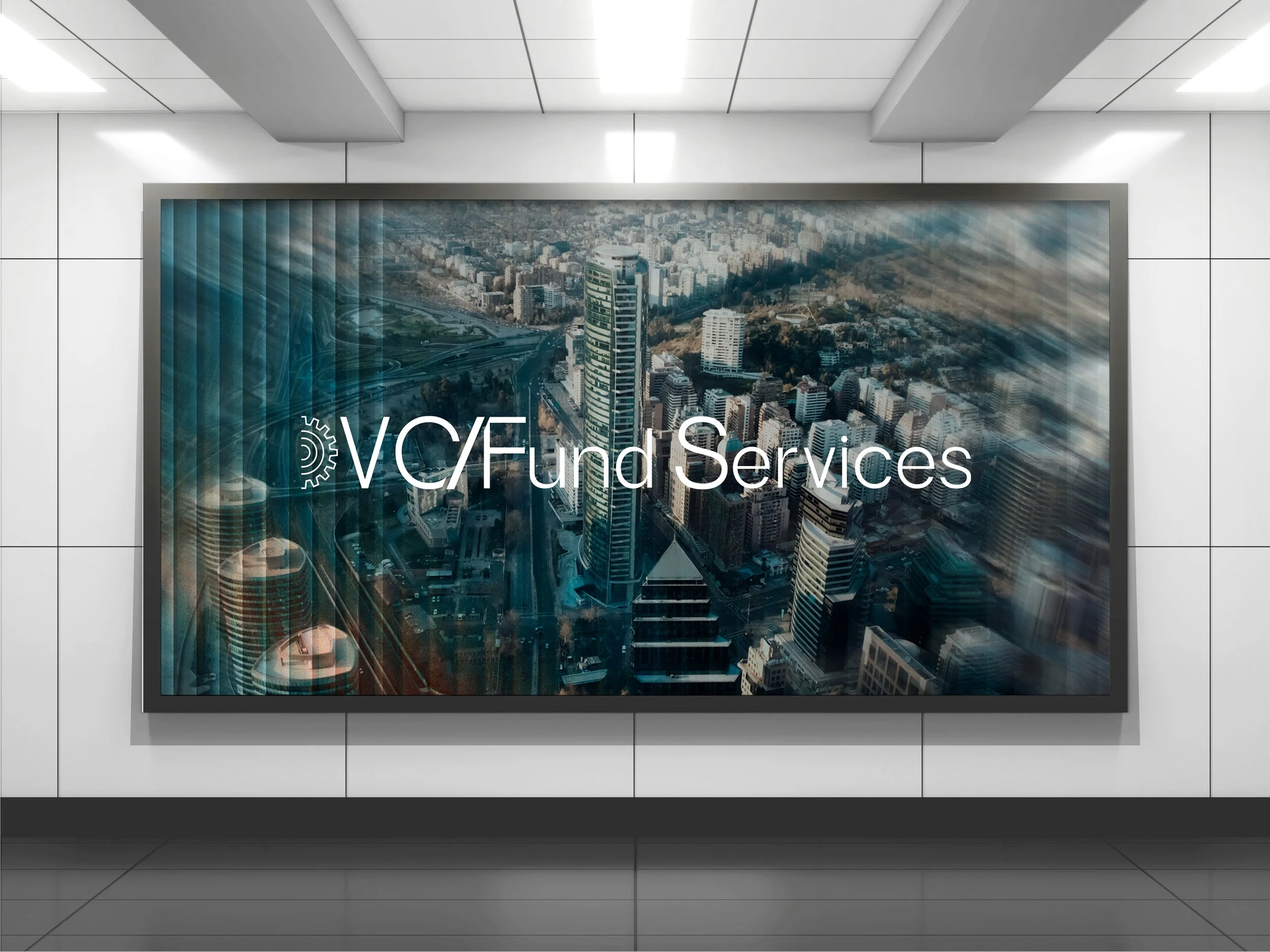 A large digital sign in a modern building lobby displays an aerial view of a city with tall skyscrapers and roads. The overlay text reads 'VCF Fund Services'.