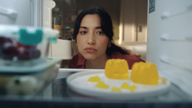 Woman looking into a refrigerator with yellow gelatin desserts on a plate inside.