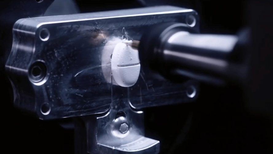A CNC machine milling a white oval-shaped object.