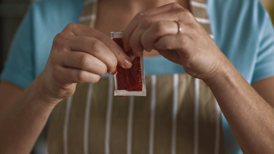 A person wearing a striped apron handling a single-use blood glucose test strip in their hands.
