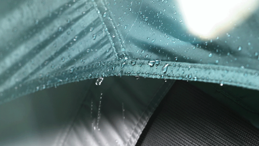 Close-up of a rain-covered fabric, possibly a tent or waterproof clothing, with water droplets on the surface.