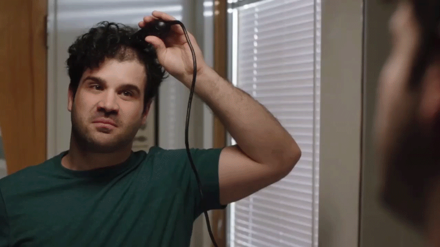 Man with curly hair looking into a mirror while using a hair curling iron.