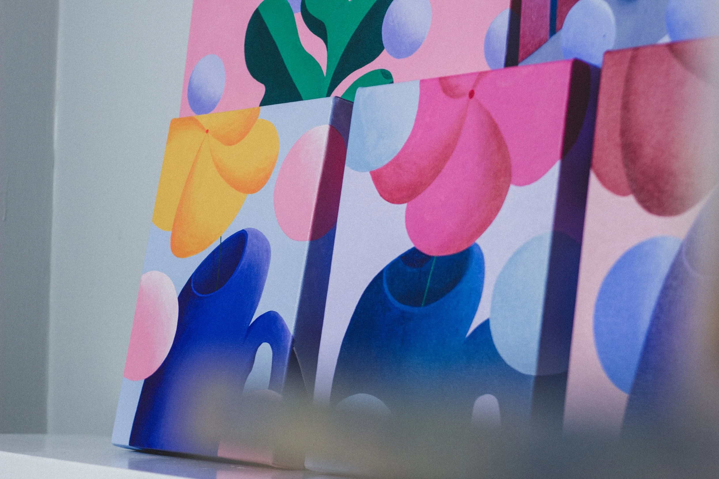 Close-up of colorful abstract artwork featuring various circles, cloud-like shapes, and bold brushstrokes in pink, blue, green, yellow, and purple on canvas.