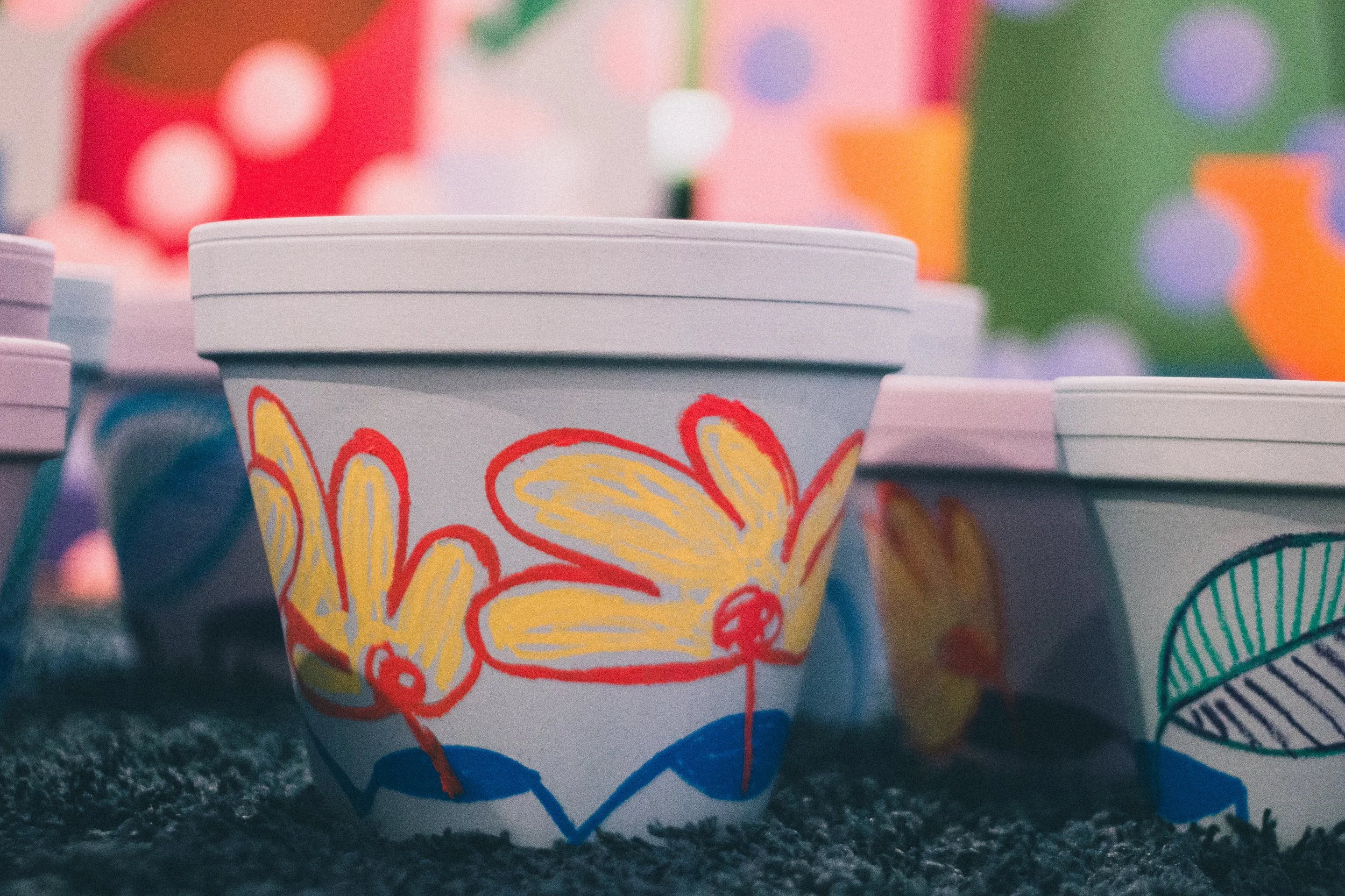 Colorful paper cups with floral and leaf designs, placed on a textured surface with a blurred colorful background.