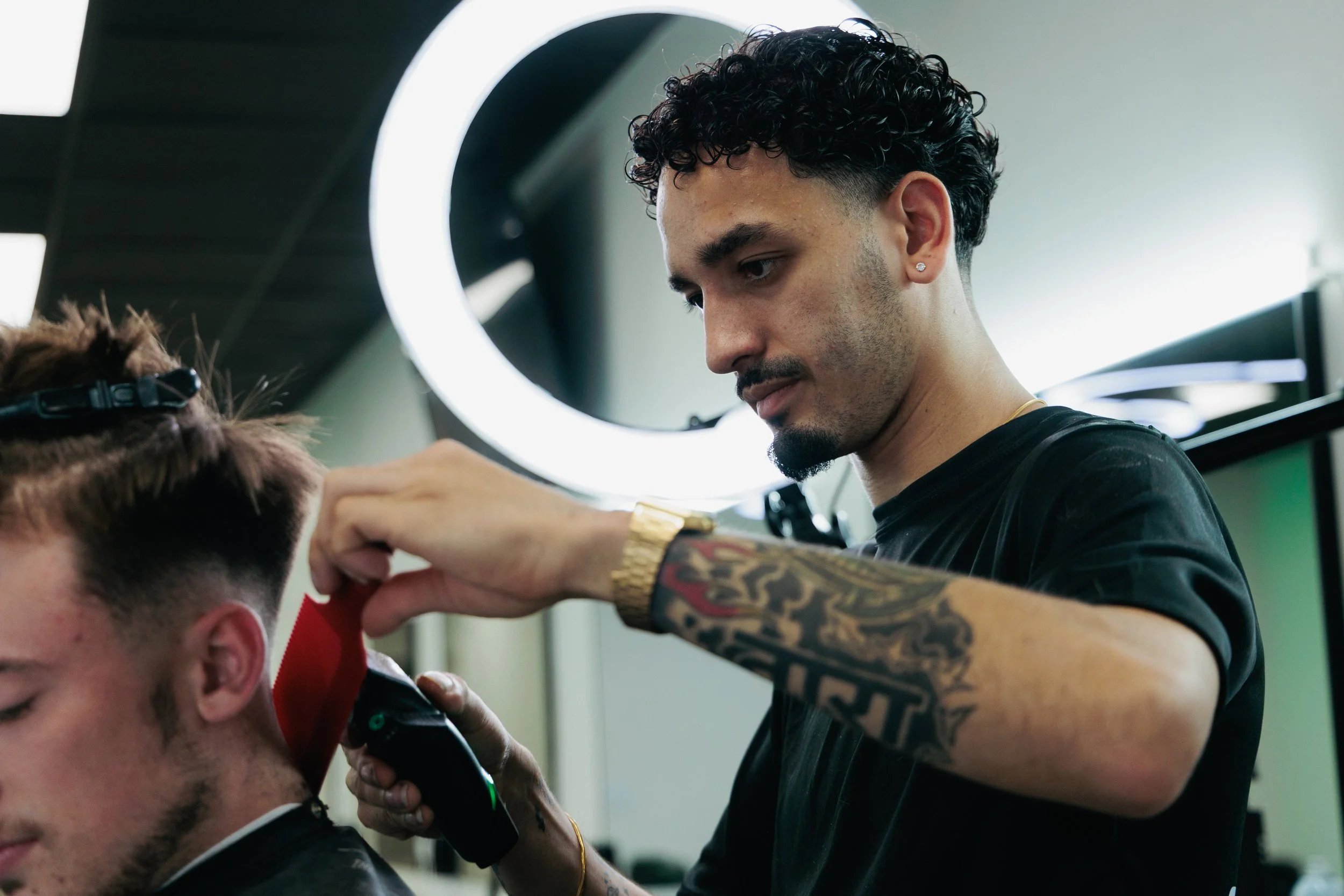 Barber giving a haircut to a young man in a salon with a circular mirror in the background.