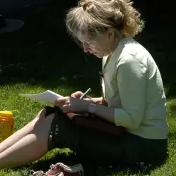 Cheryl Pallant, poet, sitting outdoors on grass, writing in a notebook.