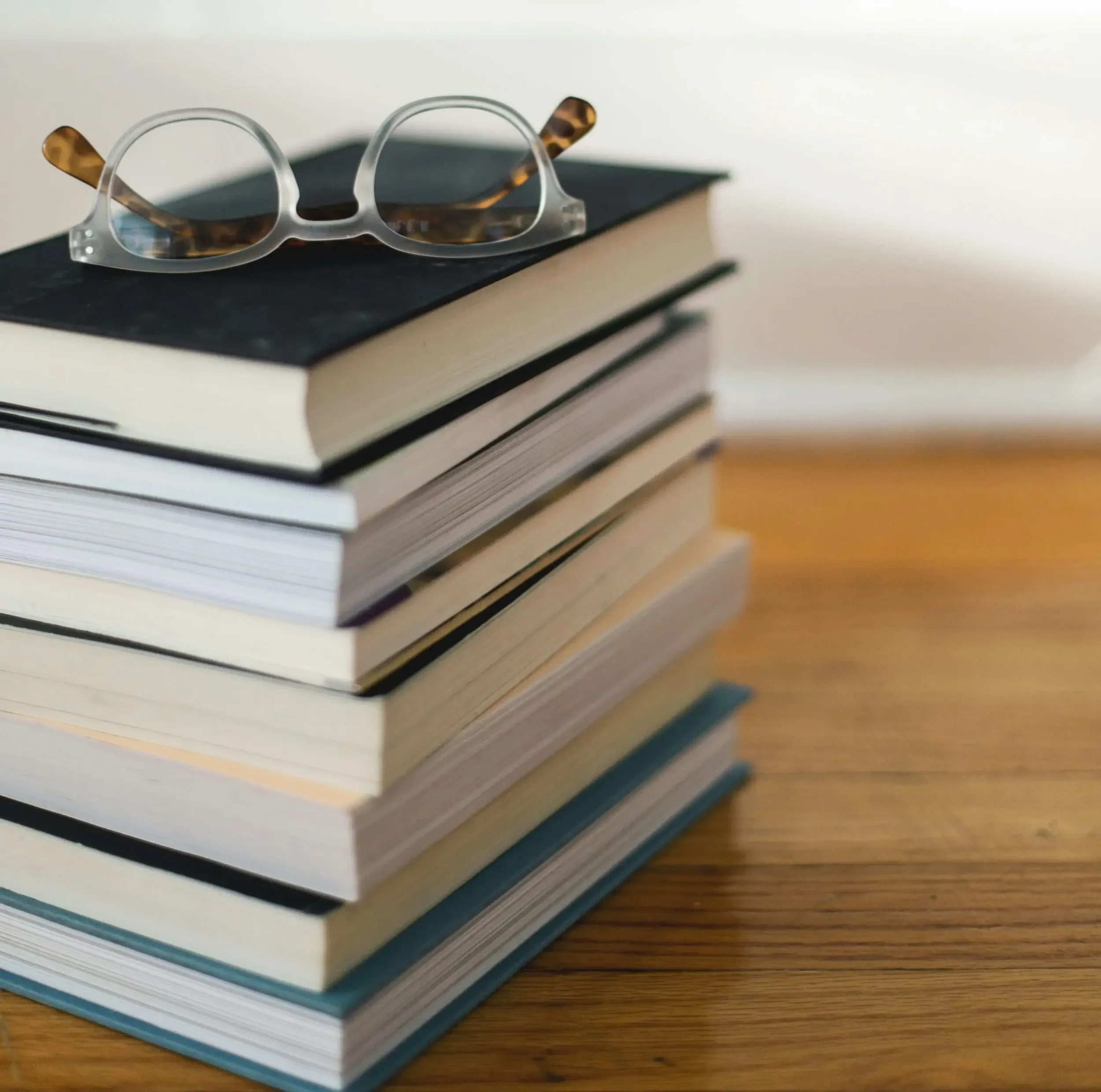 Stack of books on a wooden table with sunglasses on top.