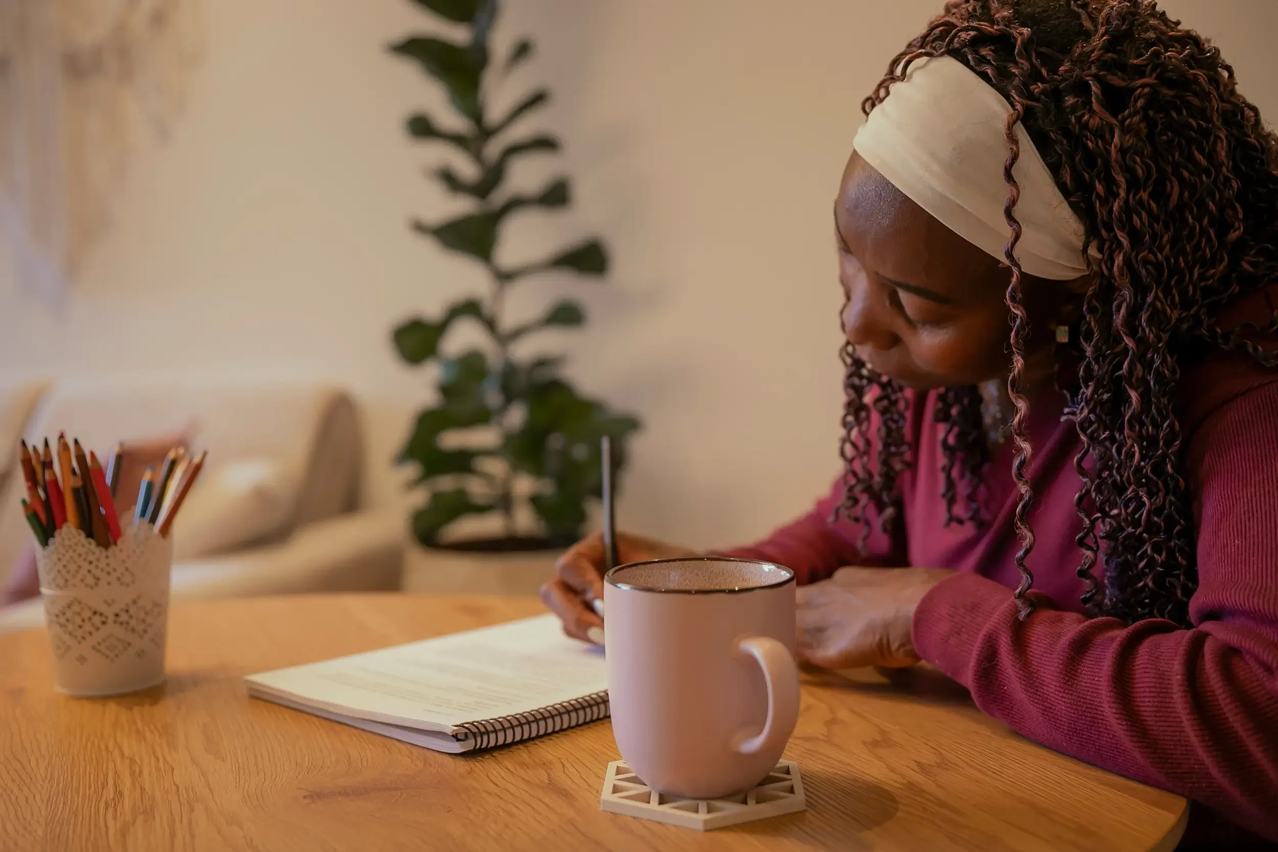 Woman with curly hair sitting at a wooden table, writing in a notebook after writing coaching with Cheryl Pallant.