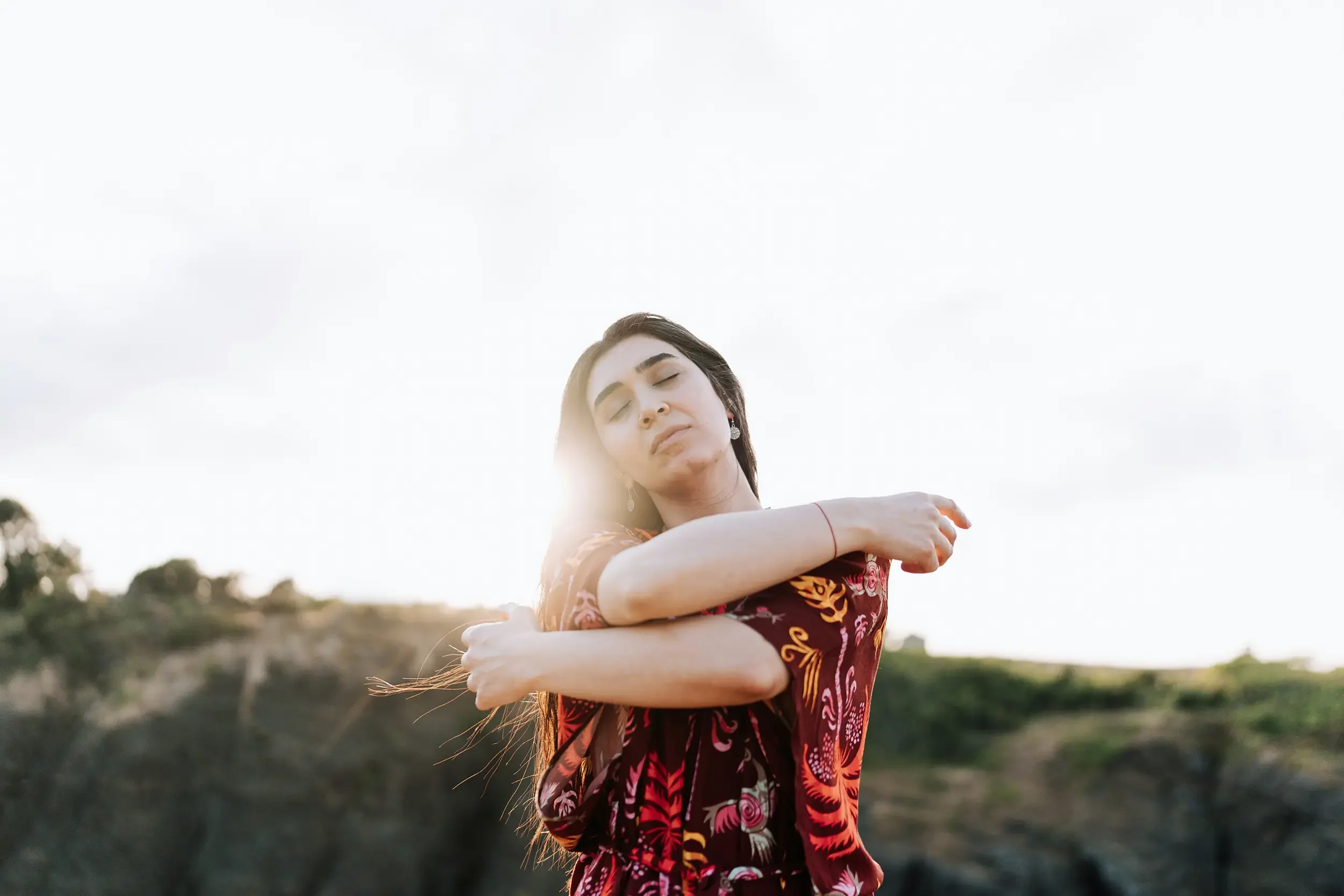 A woman with long dark hair wearing a colorful floral dress, standing outdoors during sunset during Healing Circle workshop.