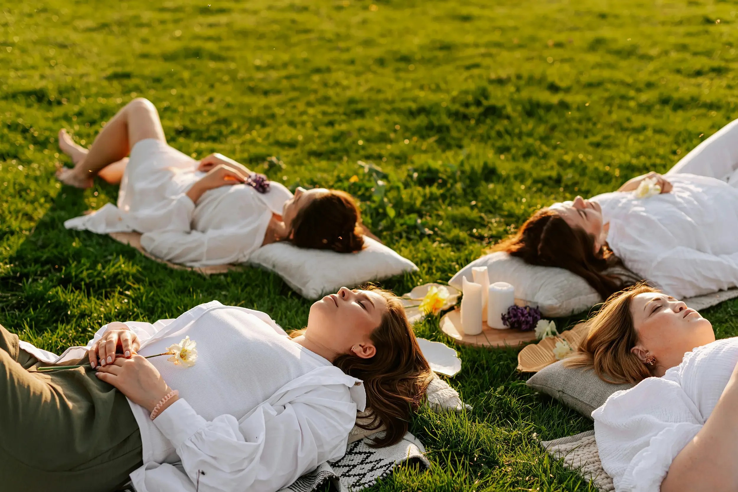 Five women lying on their backs on the grass as part of healing meditation circle workshop.