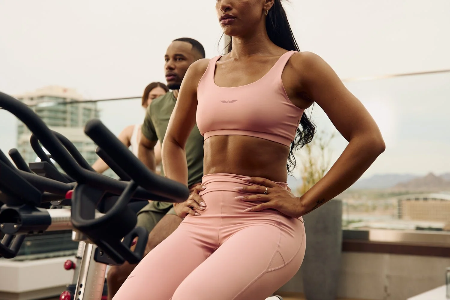 Dynamic commercial lifestyle shot of athletes in Unitus sportswear training on stationary bikes on a Tempe rooftop, capturing energy
