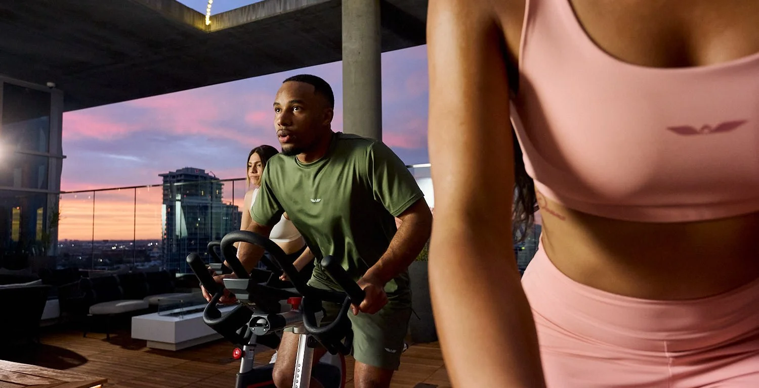 Commercial lifestyle shot of athletes in Unitus sportswear training on stationary bikes on a Tempe rooftop at sunset
