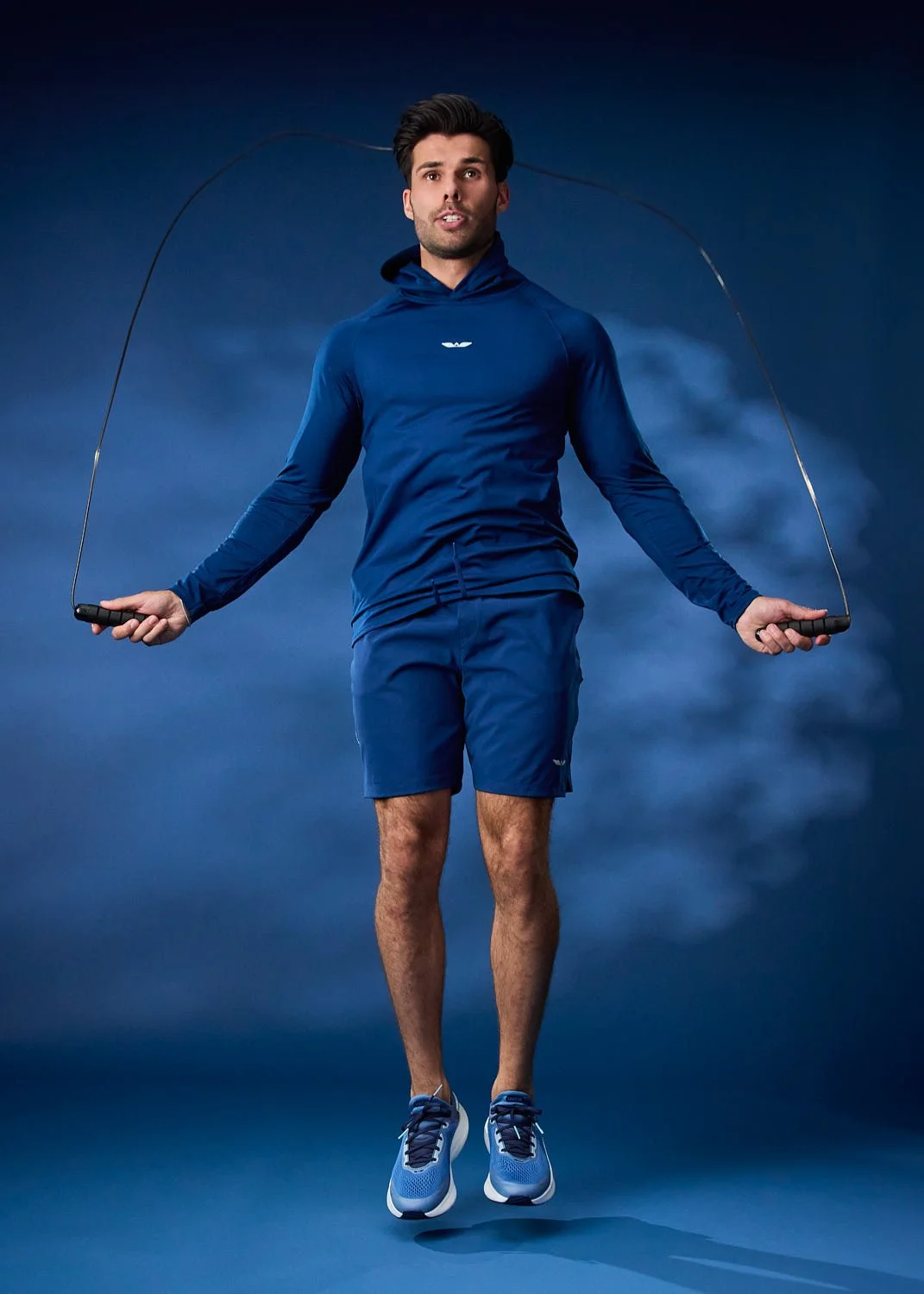 Model jump roping in blue athletic jacket on clean studio backdrop