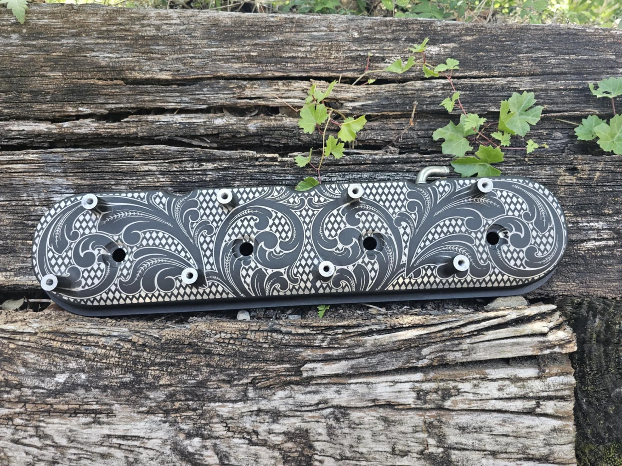 A engine cover with intricate black and white patterns, placed on a weathered wooden surface with small green leaves nearby.