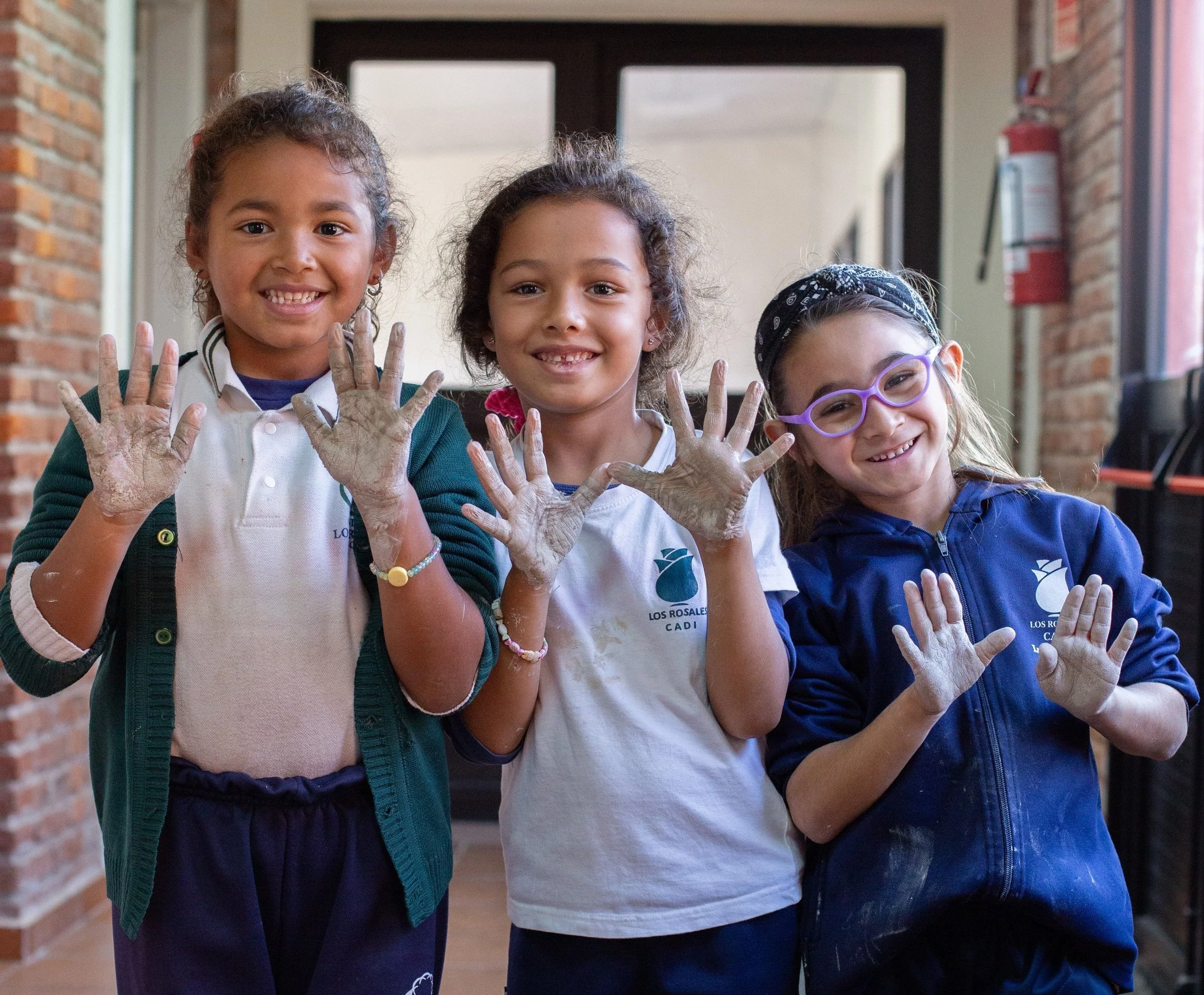 Three young girls smiling and showing their painted hands at school.