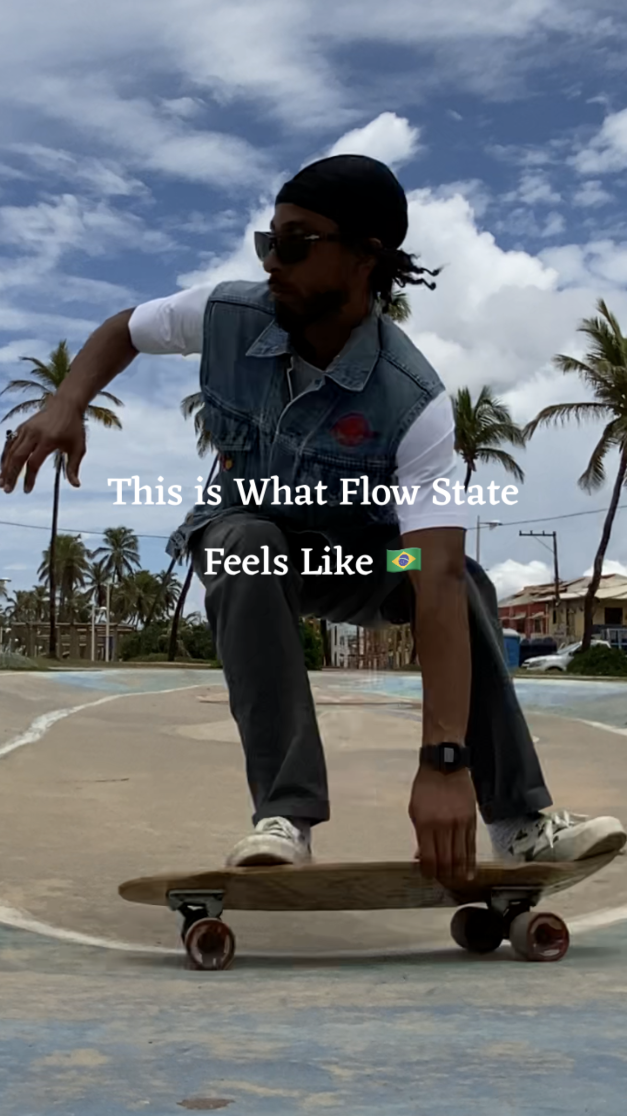 An autotelic man skateboarding outdoors on a Tony Alva board, at a skatepark in Stella Maris, Bahia. The person is wearing Persol sunglasses, a dffrntwrld® skully, a dffrntwrld® denim vest, and gray The North Face pants.
